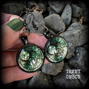 These awesome earrings feature a Dr Who inspired Gallifreyan steampunk sigil enclosed in a shiny resin dome, nice and dangly at just over 6cms from tip to tip, and weighing approx 8 grams a piece.
This pair has been made on french hooks, suitable for pierced ears.