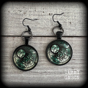 These awesome earrings feature a Dr Who inspired Gallifreyan steampunk sigil enclosed in a shiny resin dome, nice and dangly at just over 6cms from tip to tip, and weighing approx 8 grams a piece.
This pair has been made on french hooks, suitable for pierced ears.