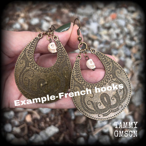 Inspired by Voodoo Sky-father Damballah, these earrings feature bone white skulls hanging from gorgeous antique bronze tear drop discs etched with a beautiful abstract serpent pattern.
Measuring 8cms from tip to tip, these unique earrings weigh 12 grams each, and have been made on antique bronze french hooks, suitable for pierced ears.