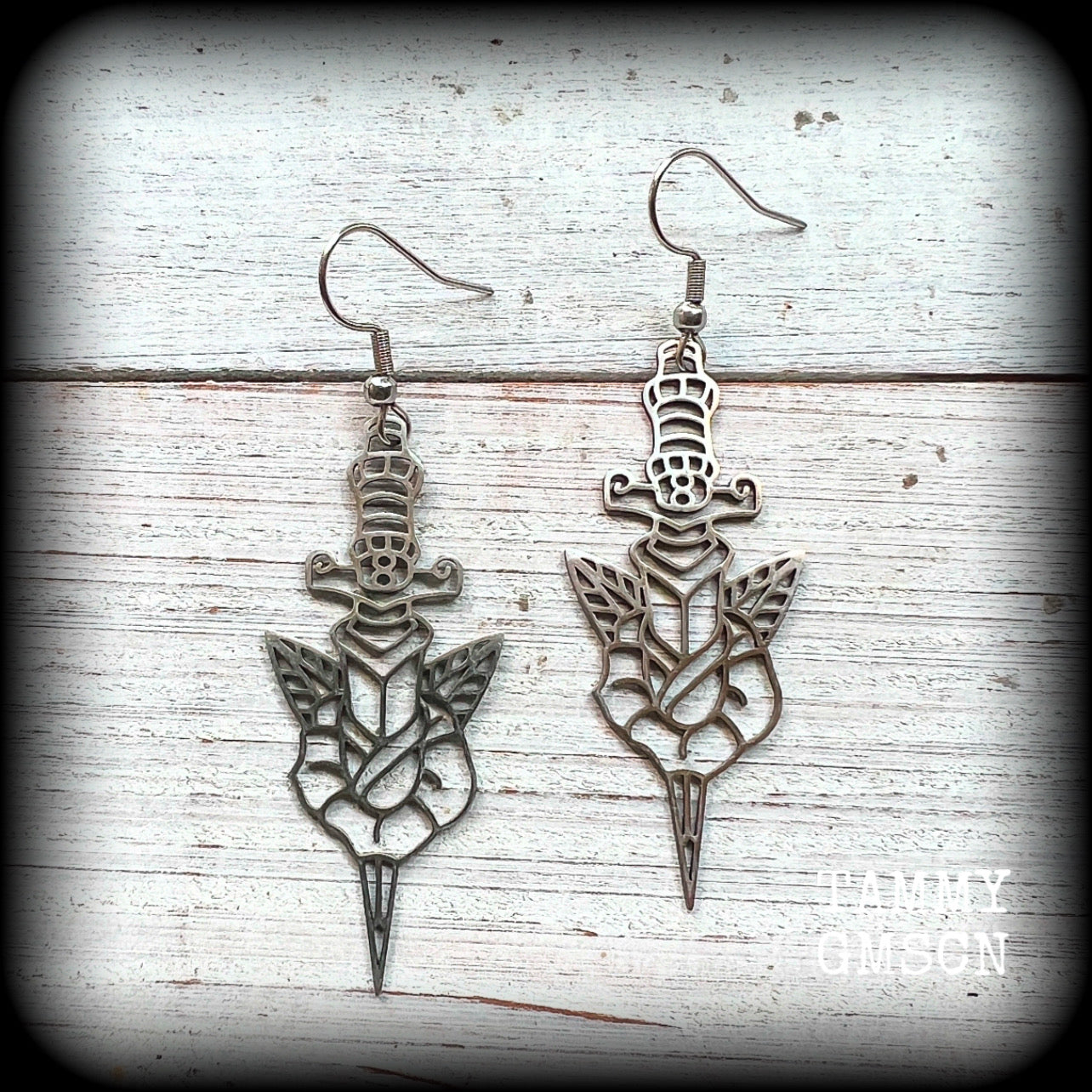 This pair of stainless steel earrings feature a classic punk rose and dagger tattoo design, measuring just on 6.5cms from tip to tip, and weighing only a grams or two each.

This pair has been made on stainless steel french hooks, suitable for pierced ears.
