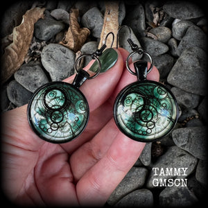 These awesome earrings feature a Dr Who inspired Gallifreyan steampunk sigil enclosed in a shiny resin dome, nice and dangly at just over 6cms from tip to tip, and weighing approx 8 grams a piece.
This pair has been made on french hooks, suitable for pierced ears.