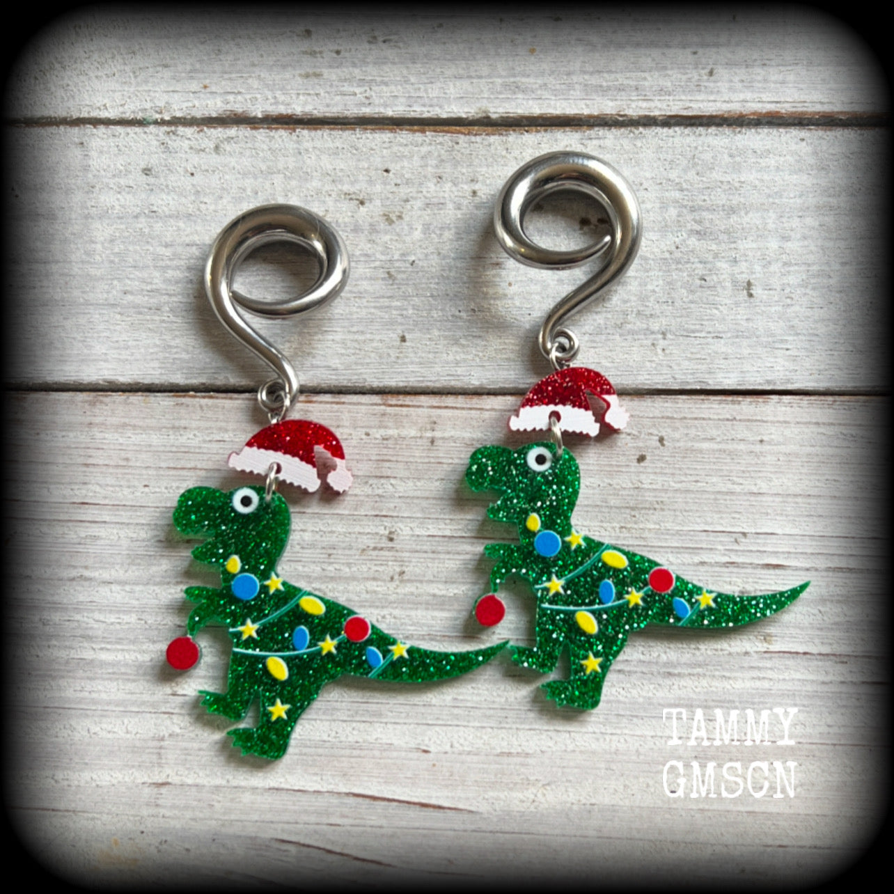 Featuring festive dinosaurs draped in colourful Christmas tree lights complete with Santa hats, these adorable earrings weigh in at 9 grams a piece, and measure approx 8cms from tip to tip.

This pair has been made on 2 gauge (6mm) surgical steel full curl hooks, to be worn in stretched lobes.