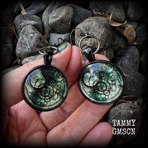 These awesome earrings feature a Dr Who inspired Gallifreyan steampunk sigil enclosed in a shiny resin dome, nice and dangly at just over 6cms from tip to tip, and weighing approx 8 grams a piece.
This pair has been made on french hooks, suitable for pierced ears.