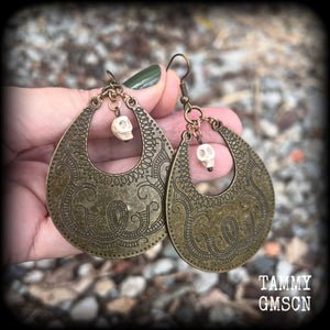 Inspired by Voodoo Sky-father Damballah, these earrings feature bone white skulls hanging from gorgeous antique bronze tear drop discs etched with a beautiful abstract serpent pattern.
Measuring 8cms from tip to tip, these unique earrings weigh 12 grams each, and have been made on antique bronze french hooks, suitable for pierced ears.