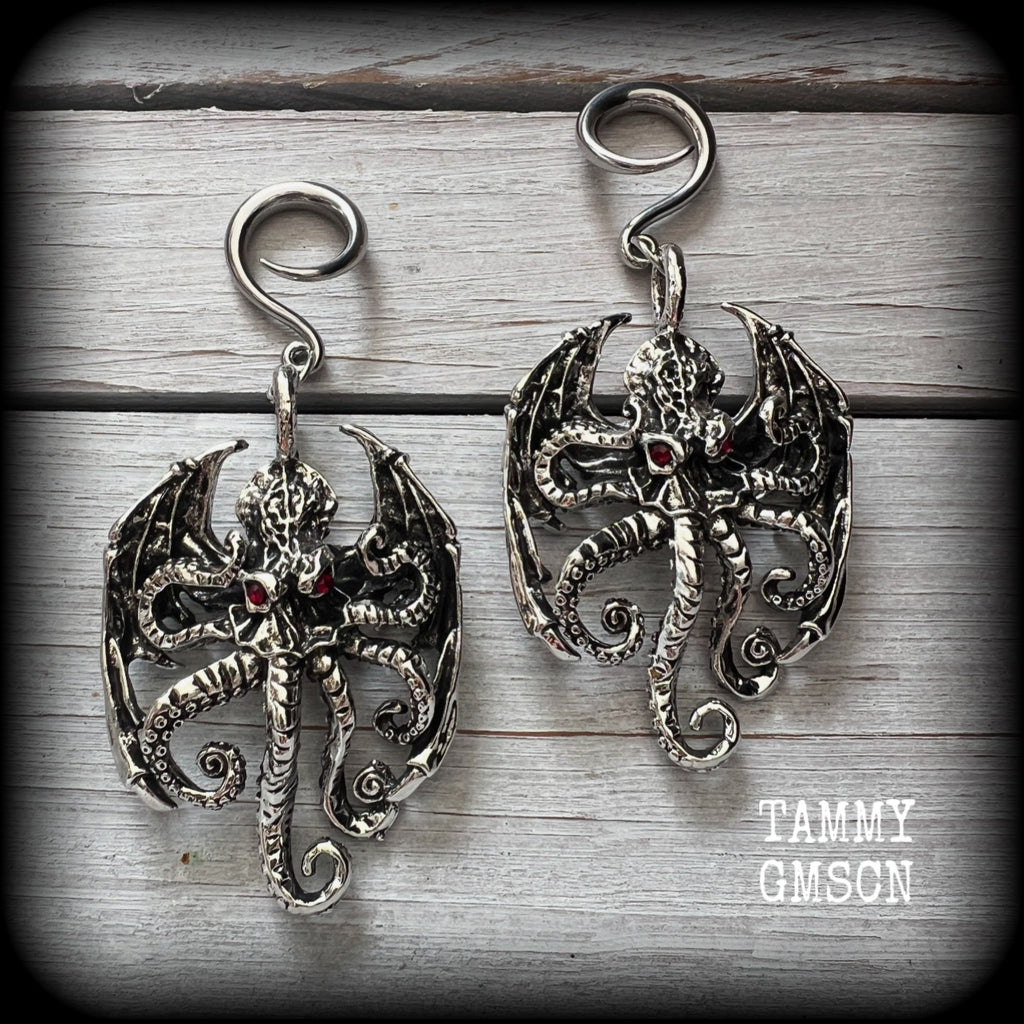 These ungodly gauged earrings feature big beautiful antique silver winged Cthulhu charms with glowing red eyes, weighing in at 27 grams a piece, and measure just over 9cms from tip to tip.

This pair has been made on 6 gauge (4mm) surgical steel full curl hooks, suitable for stretched lobes.