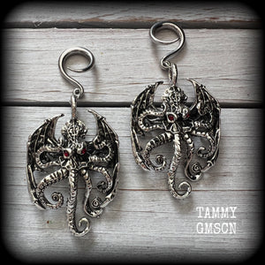 These ungodly gauged earrings feature big beautiful antique silver winged Cthulhu charms with glowing red eyes, weighing in at 27 grams a piece, and measure just over 9cms from tip to tip.

This pair has been made on 6 gauge (4mm) surgical steel full curl hooks, suitable for stretched lobes.