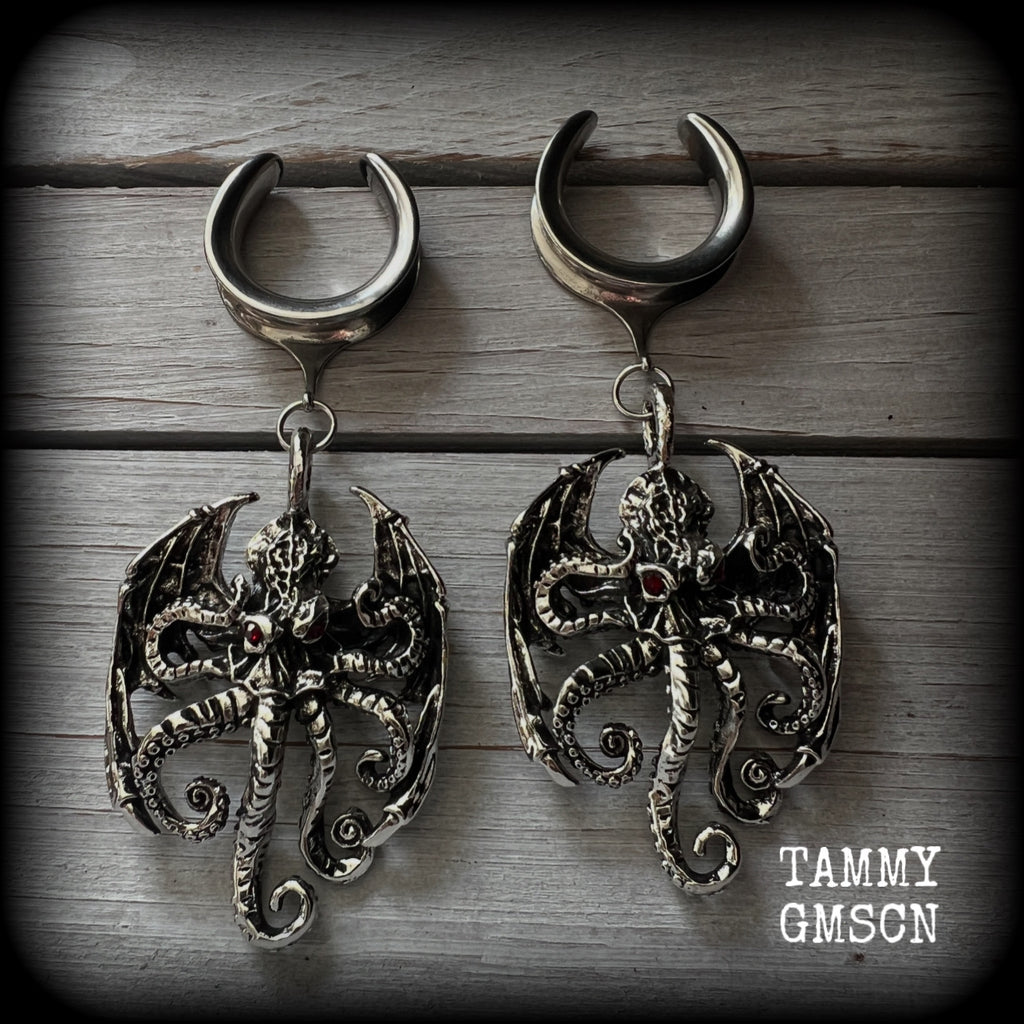 These ungodly gauged earrings feature big beautiful antique silver winged Cthulhu charms with glowing red eyes, weighing in at 33 grams a piece, and measure just over 10cms from tip to tip.

This pair has been made on 1” gauge (25mm) surgical steel full cradles, suitable for stretched lobes.