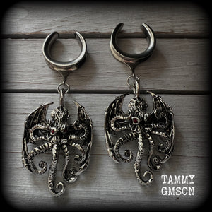 These ungodly gauged earrings feature big beautiful antique silver winged Cthulhu charms with glowing red eyes, weighing in at 33 grams a piece, and measure just over 10cms from tip to tip.

This pair has been made on 1” gauge (25mm) surgical steel full cradles, suitable for stretched lobes.