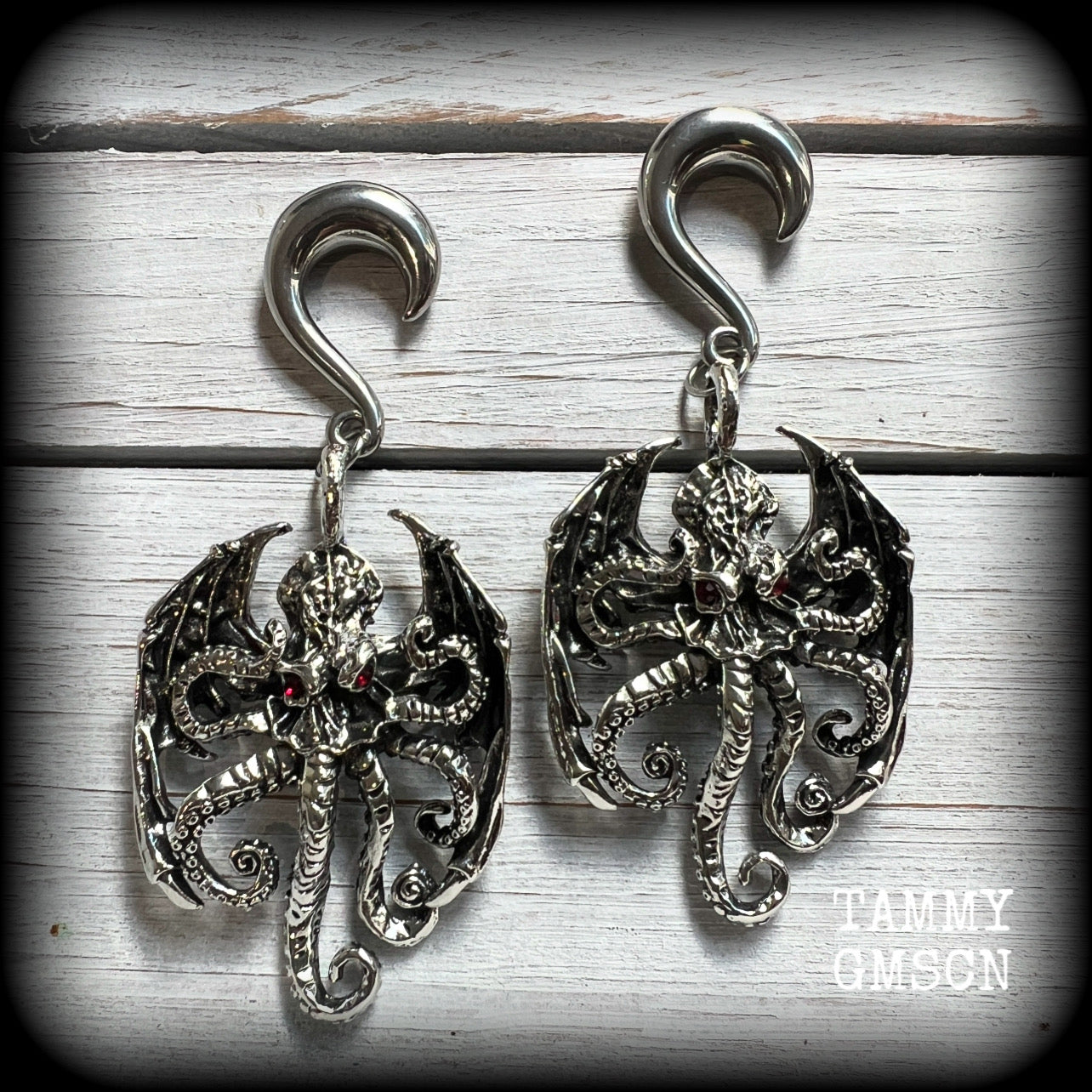 These ungodly gauged earrings feature big beautiful antique silver winged Cthulhu charms with glowing red eyes, weighing in at 33 grams a piece, and measure just on 9.5cms from tip to tip.

This pair has been made on 0 gauge (8mm) surgical steel half curl hooks, suitable for stretched lobes.