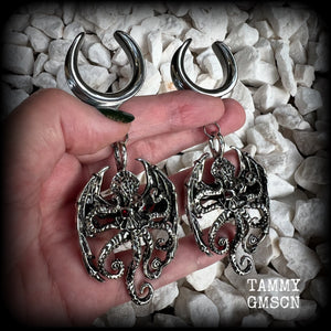 These ungodly gauged earrings feature big beautiful antique silver winged Cthulhu charms with glowing red eyes, weighing in at 33 grams a piece, and measure just over 10cms from tip to tip.  This pair has been made on 1” gauge (25mm) surgical steel full cradles, suitable for stretched lobes.