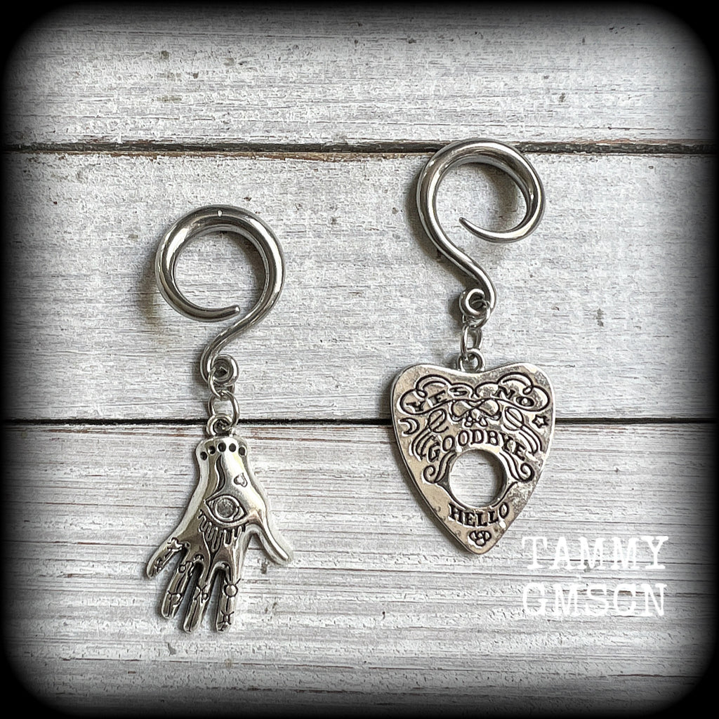 Featuring an antique silver Ouija planchette and esoteric hand charm, this pair of gorgeous earrings weigh approx 5 grams a piece, and measure 6cms from tip to tip.

This pair has been made on 6 gauge (4mm) surgical steel full curl hooks, suitable for stretched lobes.

