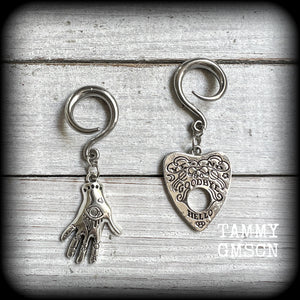 Featuring an antique silver Ouija planchette and esoteric hand charm, this pair of gorgeous earrings weigh approx 5 grams a piece, and measure 6cms from tip to tip.

This pair has been made on 6 gauge (4mm) surgical steel full curl hooks, suitable for stretched lobes.

