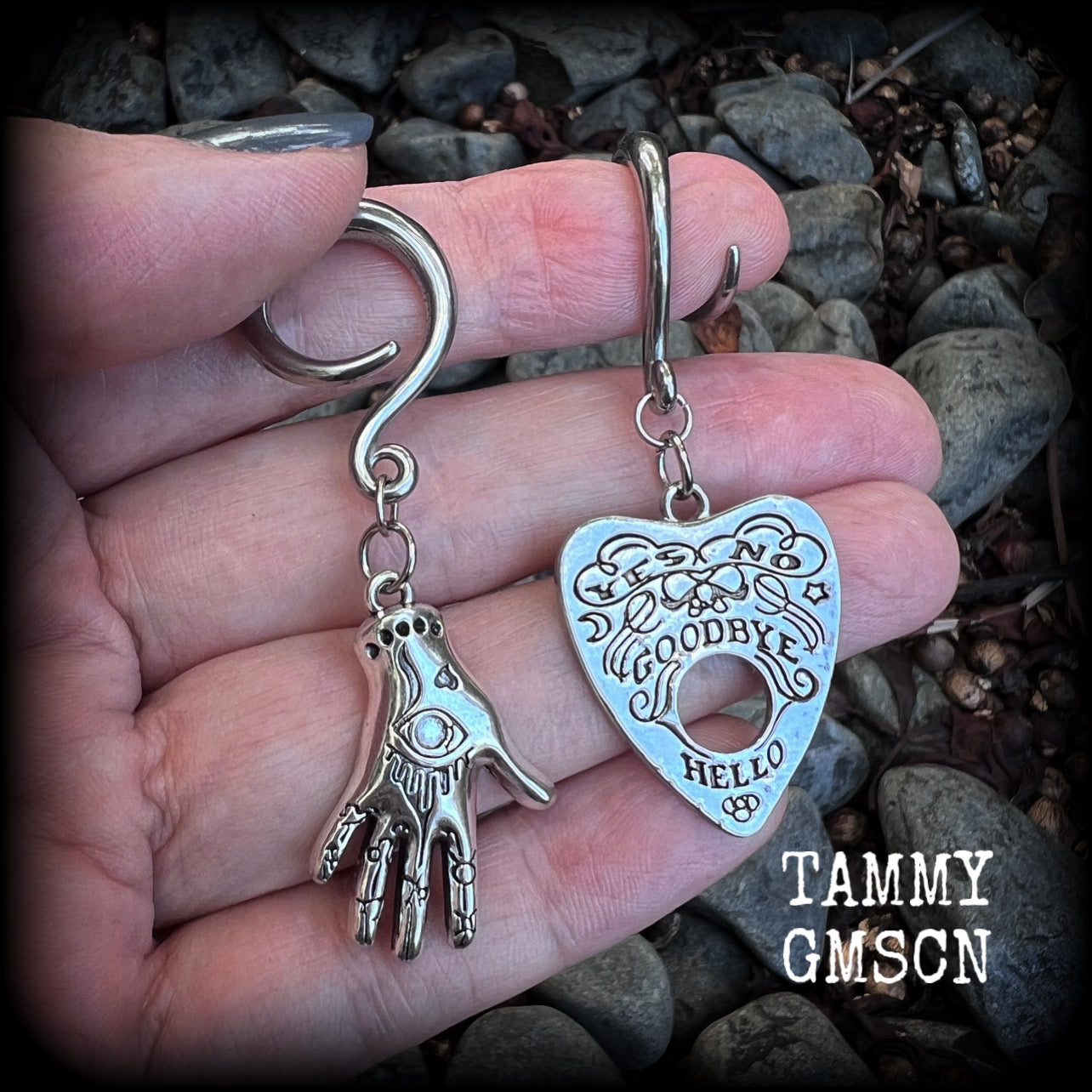 Featuring an antique silver Ouija planchette and esoteric hand charm, this pair of gorgeous earrings weigh approx 5 grams a piece, and measure 6cms from tip to tip.

This pair has been made on 6 gauge (4mm) surgical steel full curl hooks, suitable for stretched lobes.

