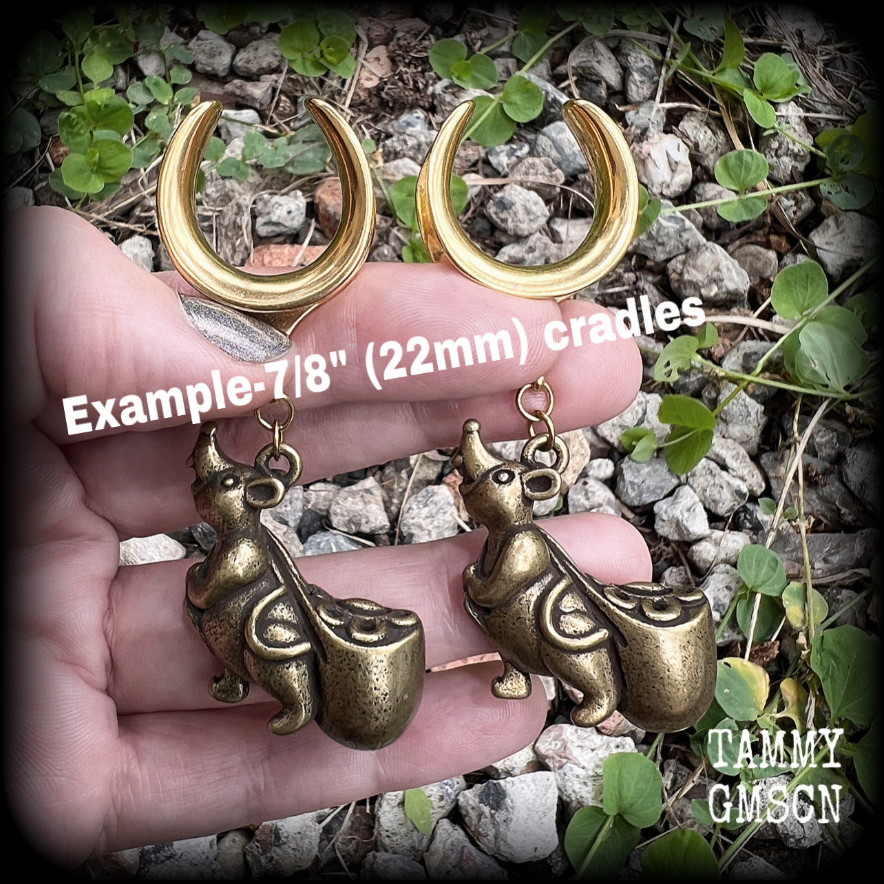 May include: Two gold-colored ear gauges with a dangling chinese money rat charm. Each rat charm is holding a small, round, gold-colored bag. The text 'TAMMY GMSCN' is visible at the bottom of the image.