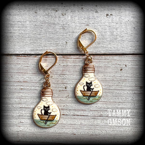 These cute quirky earrings feature a black cat rowing a little row boat down the stream under a cloudy sky. This pair of earrings can be made on your choice of hooks and clasps for pierced ears or stretched lobes.