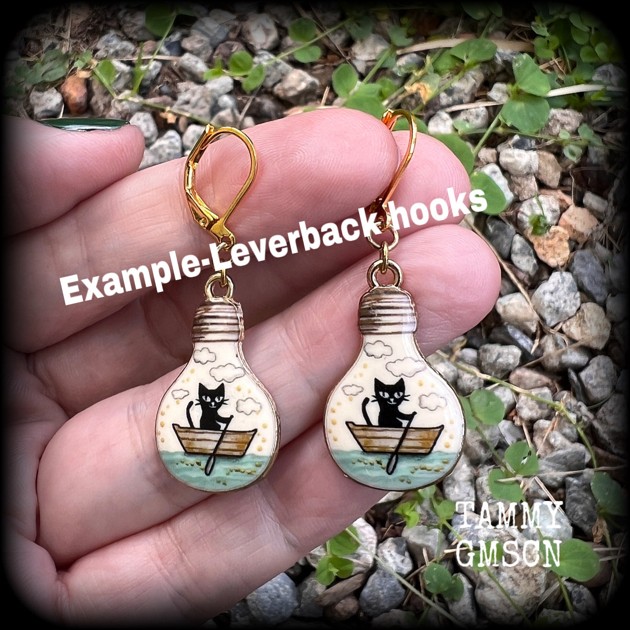 These cute quirky earrings feature a black cat rowing a little row boat down the stream under a cloudy sky. This pair of earrings can be made on your choice of hooks and clasps for pierced ears or stretched lobes.