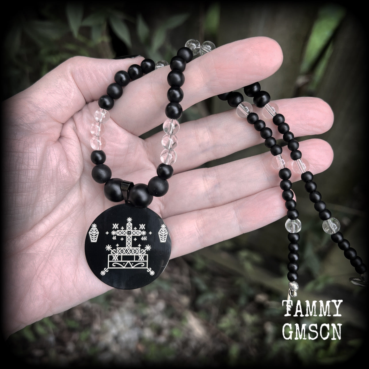 This necklace features gorgeous glass and matte black obsidian beads, with a large engraved enamel veve pendant, inspired by Baron Samedi.

This necklace measures approx 40cms when laying flat, and fastens with an antique silver toggle clasp.