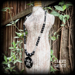 This necklace features gorgeous glass and matte black obsidian beads, with a large engraved enamel veve pendant, inspired by Baron Samedi.

This necklace measures approx 40cms when laying flat, and fastens with an antique silver toggle clasp.