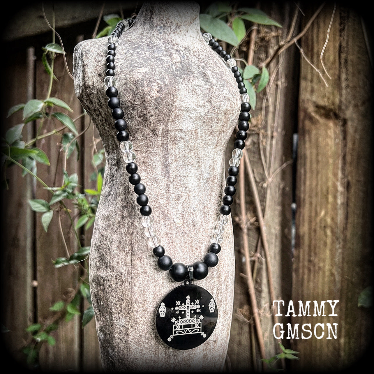 This necklace features gorgeous glass and matte black obsidian beads, with a large engraved enamel veve pendant, inspired by Baron Samedi.

This necklace measures approx 40cms when laying flat, and fastens with an antique silver toggle clasp.