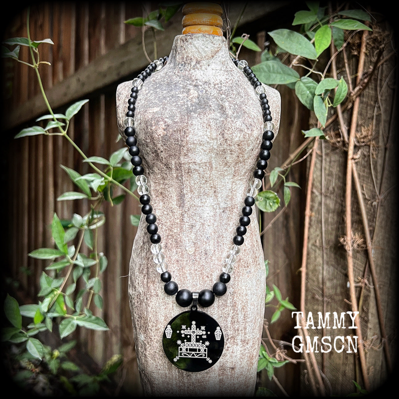 This necklace features gorgeous glass and matte black obsidian beads, with a large engraved enamel veve pendant, inspired by Baron Samedi.

This necklace measures approx 40cms when laying flat, and fastens with an antique silver toggle clasp.