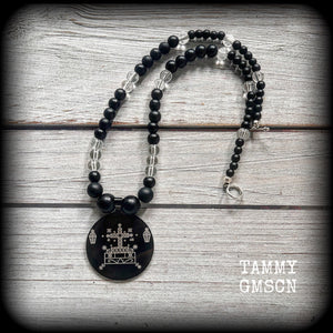 This necklace features gorgeous glass and matte black obsidian beads, with a large engraved enamel veve pendant, inspired by Baron Samedi.

This necklace measures approx 40cms when laying flat, and fastens with an antique silver toggle clasp.