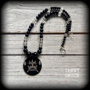 This necklace features gorgeous glass and matte black obsidian beads, with a large engraved enamel veve pendant, inspired by Baron Samedi.

This necklace measures approx 40cms when laying flat, and fastens with an antique silver toggle clasp.