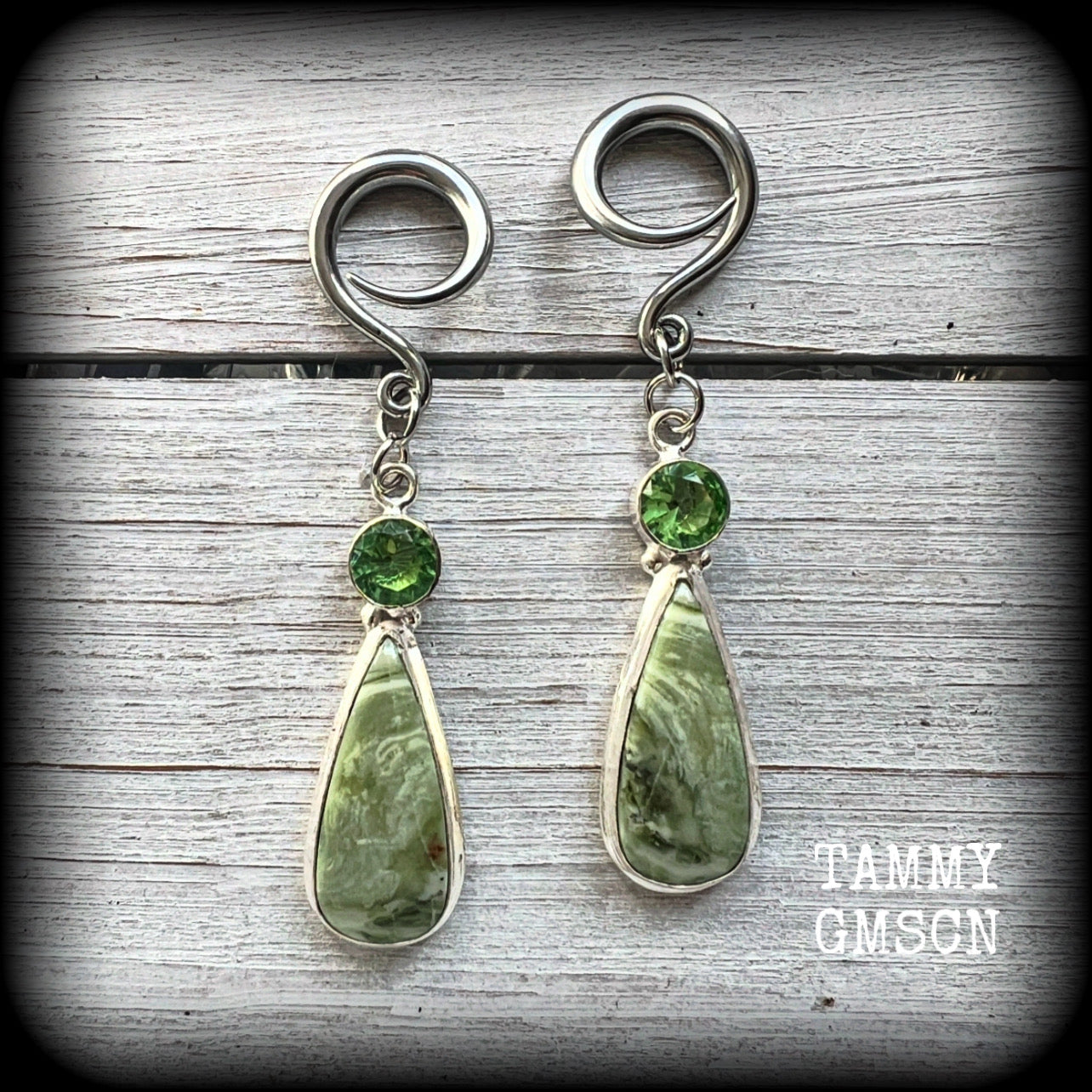 These beautiful Serpentine and green garnet earrings are made with gorgeous polished and faceted gemstones, lovely and dangly measuring just approx 7.5cms from tip to tip, and weighing approx 9 grams each. 

These earrings have been made on 6 gauge (4mm) surgical steel full curl hooks, to be worn in stretched lobes.
