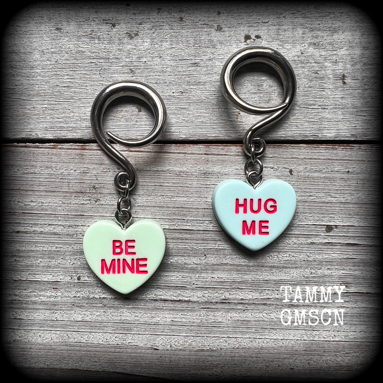 These adorable candy heart ear hangers feature mismatched Be mine and Hug me candy hearts, measuring just under 5cms from tip to tip, and weighing only a few grams each.
This pair has been made on 6 gauge (4mm) surgical steel full curl hooks, suitable for stretched lobes.
