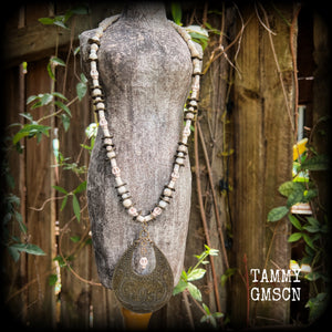 This unique necklace features a gorgeous antique bronze abstract snake pendant with a small bone white howlite stone skull dangling atop, on a strand of bone white stone and ornate antique bronze beads.
This necklace measures 44cms from tip to tip when laid flat and fastens with an antique bronze lobster clasp.