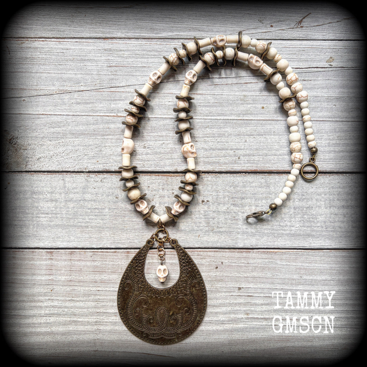 This unique necklace features a gorgeous antique bronze abstract snake pendant with a small bone white howlite stone skull dangling atop, on a strand of bone white stone and ornate antique bronze beads.
This necklace measures 44cms from tip to tip when laid flat and fastens with an antique bronze lobster clasp.