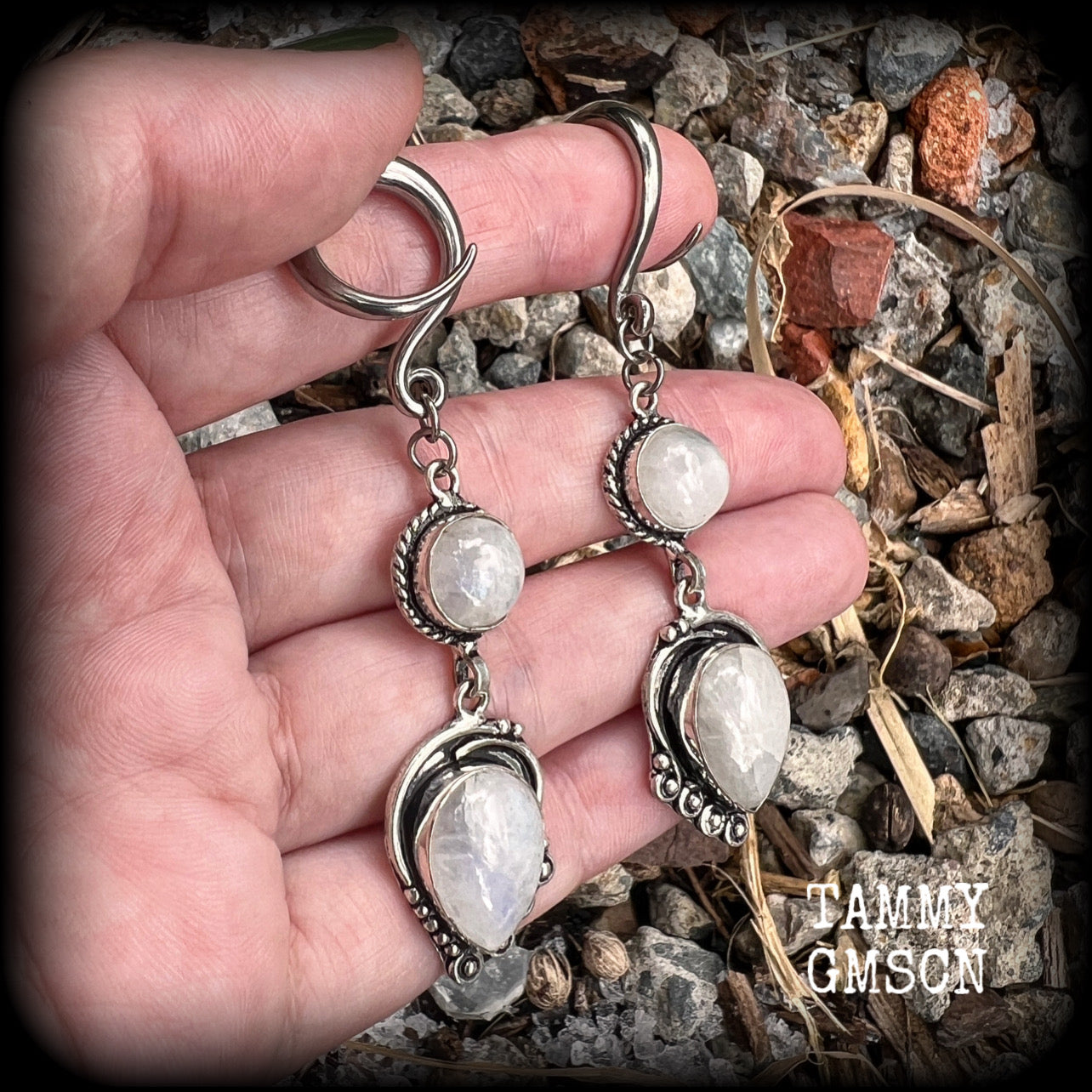 These gorgeous earrings feature polished Rainbow Moonstone gemstones in a beautiful boho antique silver setting, lovely and dangly at approx 8cms from tip to tip, and not too heavy at 9 grams each.
This pair had been made on 6 gauge (4mm) surgical steel full curl hooks, to be worn in stretched lobes.