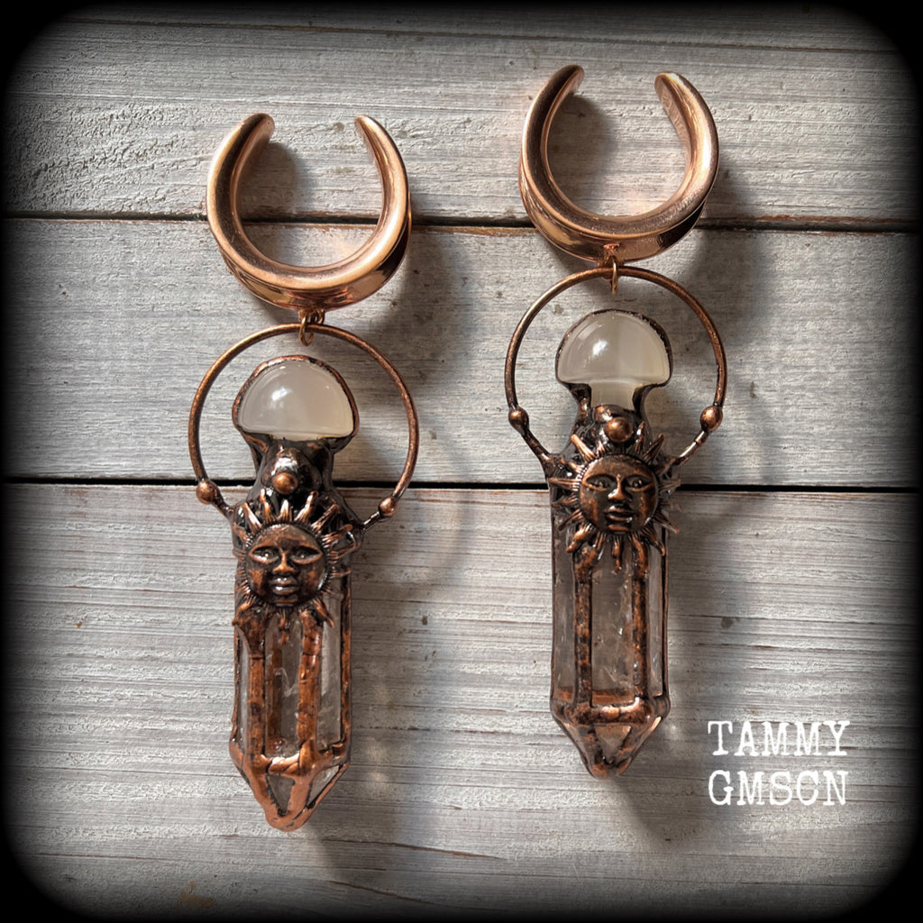 These unique ear weights feature big clear quartz points enclosed in a copper electroplate cage with topped with folk horror inspired celestial suns. These gorgeous earrings measure 11cms from tip to tip, and weigh approx 45 grams each.
This pair has been made on 1” gauge (25mm) rose gold tone surgical steel cradles, suitable for stretched lobes.