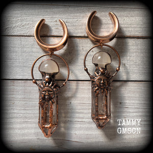 These unique ear weights feature big clear quartz points enclosed in a copper electroplate cage with topped with folk horror inspired celestial suns. These gorgeous earrings measure 11cms from tip to tip, and weigh approx 45 grams each.
This pair has been made on 1” gauge (25mm) rose gold tone surgical steel cradles, suitable for stretched lobes.