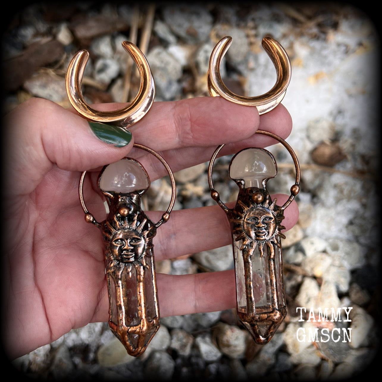 These unique ear weights feature big clear quartz points enclosed in a copper electroplate cage with topped with folk horror inspired celestial suns. These gorgeous earrings measure 11cms from tip to tip, and weigh approx 45 grams each.
This pair has been made on 1” gauge (25mm) rose gold tone surgical steel cradles, suitable for stretched lobes.