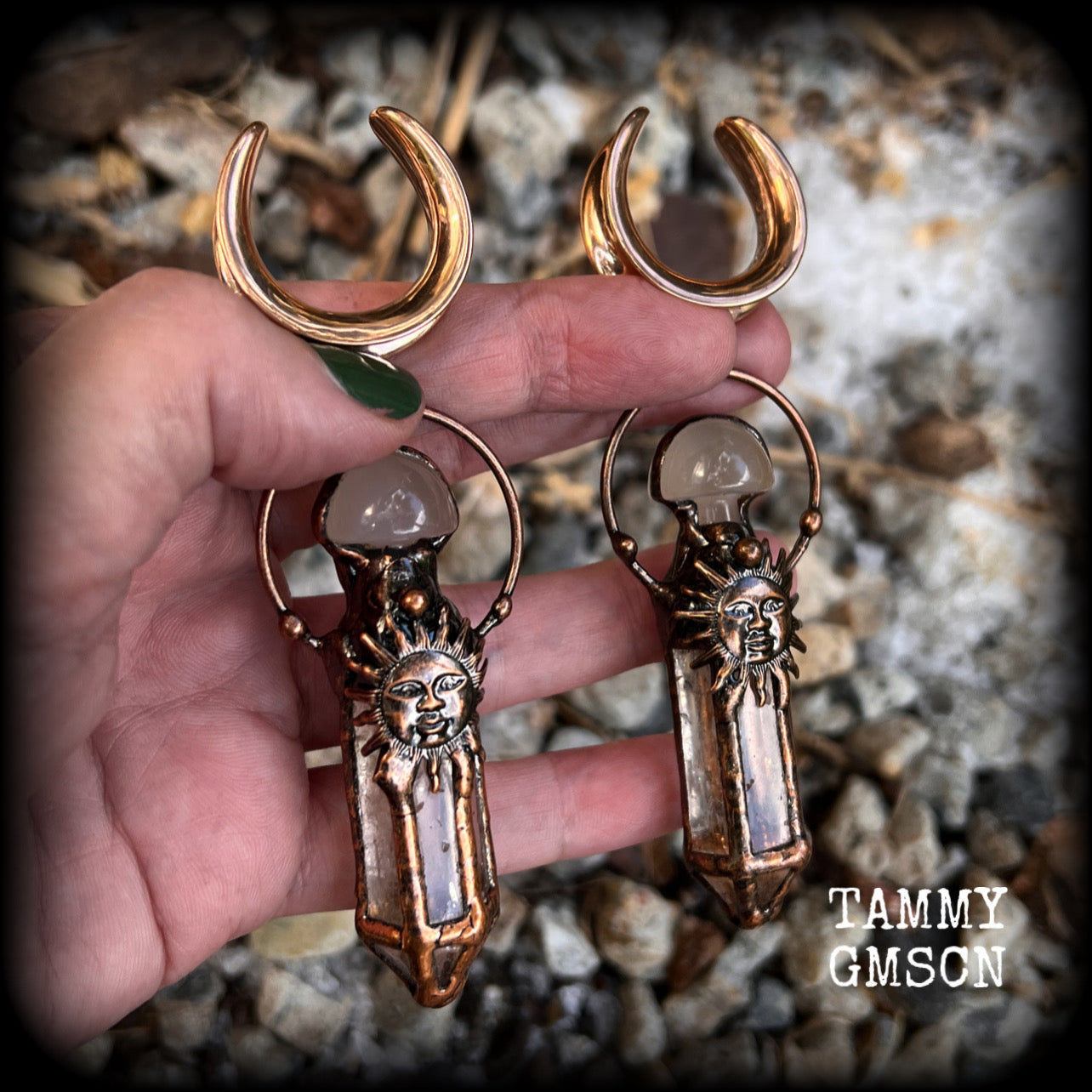 These unique ear weights feature big clear quartz points enclosed in a copper electroplate cage with topped with folk horror inspired celestial suns. These gorgeous earrings measure 11cms from tip to tip, and weigh approx 45 grams each.
This pair has been made on 1” gauge (25mm) rose gold tone surgical steel cradles, suitable for stretched lobes.