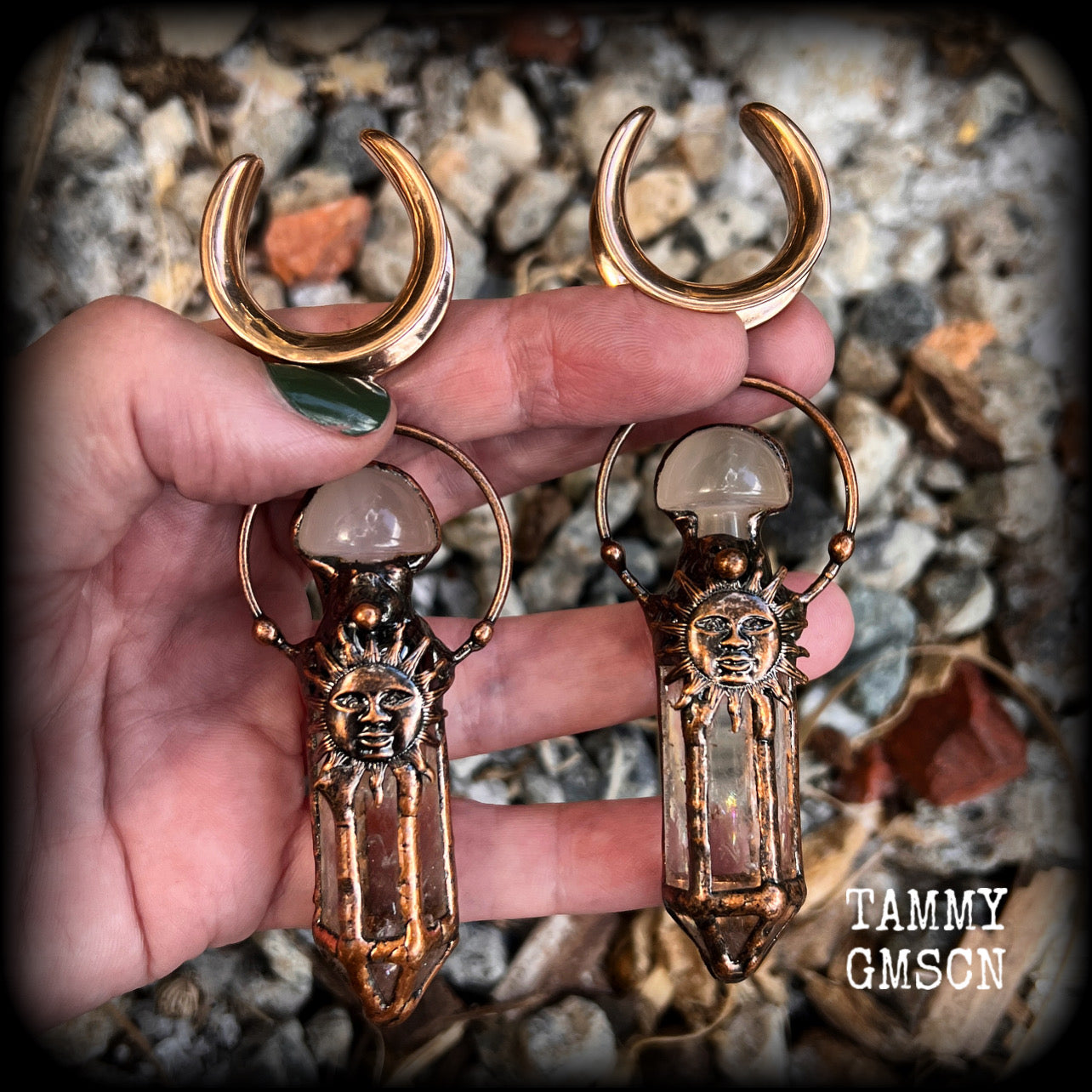 These unique ear weights feature big clear quartz points enclosed in a copper electroplate cage with topped with folk horror inspired celestial suns. These gorgeous earrings measure 11cms from tip to tip, and weigh approx 45 grams each.
This pair has been made on 1” gauge (25mm) rose gold tone surgical steel cradles, suitable for stretched lobes.