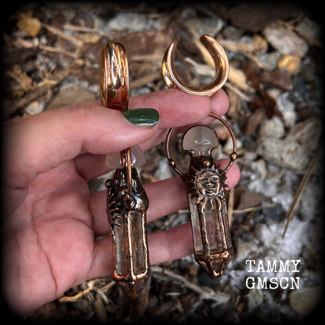 These unique ear weights feature big clear quartz points enclosed in a copper electroplate cage with topped with folk horror inspired celestial suns. These gorgeous earrings measure 11cms from tip to tip, and weigh approx 45 grams each.
This pair has been made on 1” gauge (25mm) rose gold tone surgical steel cradles, suitable for stretched lobes.