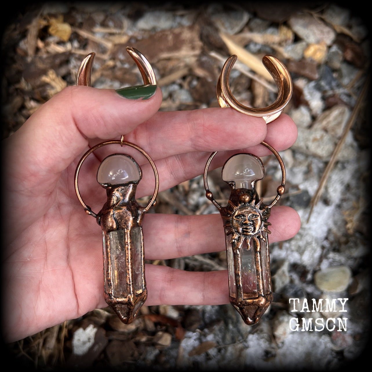 These unique ear weights feature big clear quartz points enclosed in a copper electroplate cage with topped with folk horror inspired celestial suns. These gorgeous earrings measure 11cms from tip to tip, and weigh approx 45 grams each.
This pair has been made on 1” gauge (25mm) rose gold tone surgical steel cradles, suitable for stretched lobes.