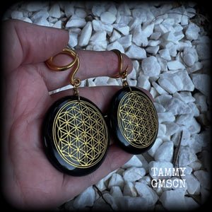 These beautiful ear hangers feature gorgeous pitch black obsidian gemstones etched with a beautiful gold flower of life motif, measuring just over 7cms from tip to tip, and weighing approx 24 grams each.

This pair has been made on 6 gauge (4mm) surgical steel full curl hooks, to be worn in stretched lobes.