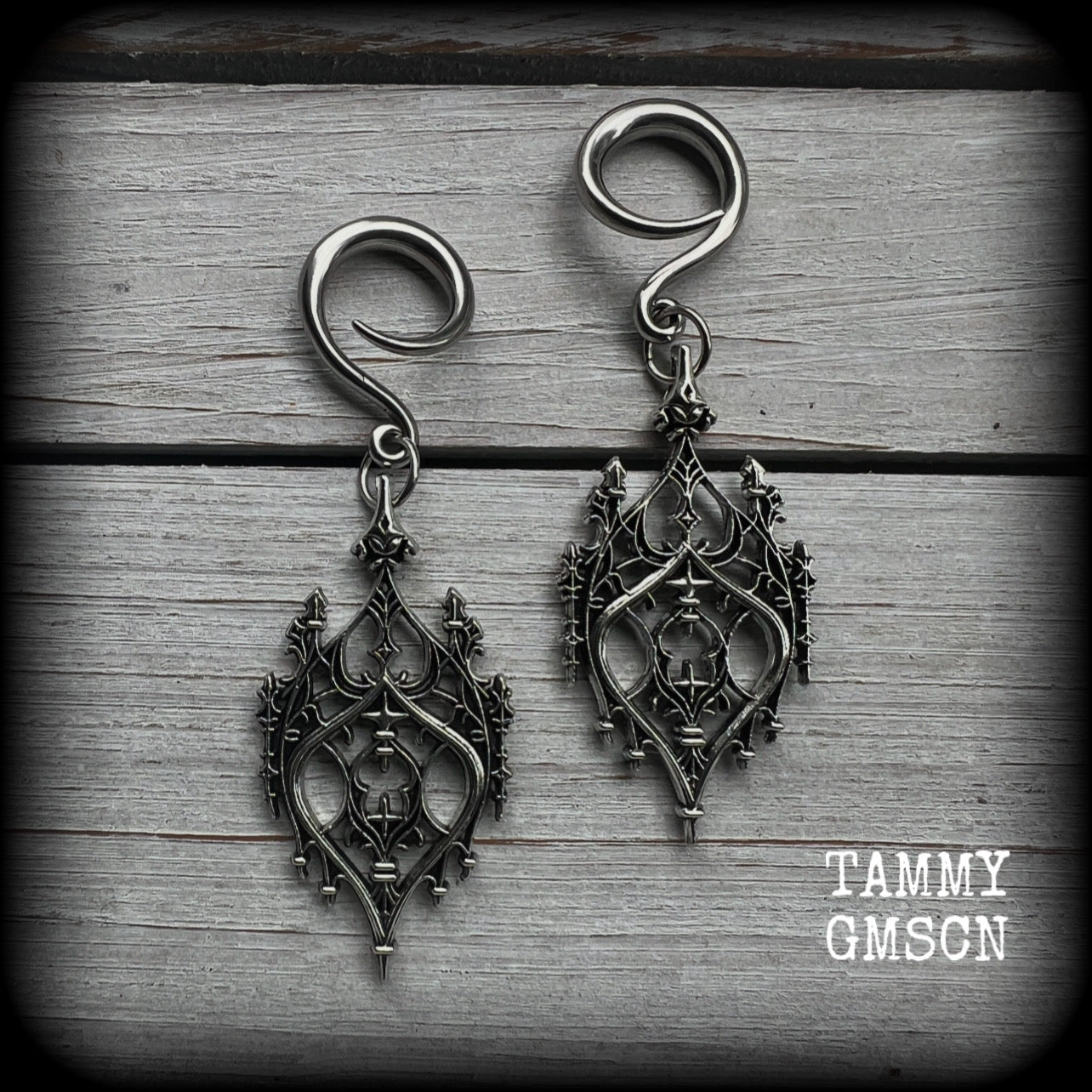 These gorgeous gothic ear hangers feature a beautiful antique silver ornate gothic cathedral chandelier, measuring just on 8cms from tip to tip, and weighing approx 10 grams each.
This pair has been made on 6 gauge (4mm) surgical steel full curls, to be worn in stretched lobes.
