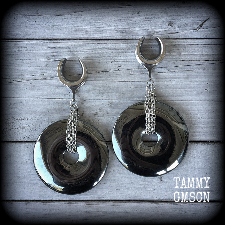 Hematite ear weights This is a pair of shiny black hematite donut gemstones with antique silver chain, weighing approx 50 grams a piece and measure just on 9cms from tip to tip.
This pair has been made on 5/8" gauge (16mm) surgical steel cradles,  for stretched lobes.