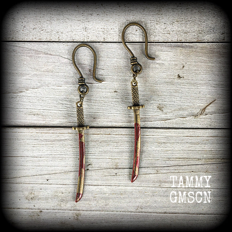 Featuring bloodied antique bronze swords, these earrings are symbolic of the severing of the bondage of ignorance and ego.

Measuring 8cms from tip to tip, these earrings are nice and light weight, weighing only a gram or 2 each.

This pair has been made with small antique bronze shephard hooks, suitable to be worn in stretched lobes with silicone earlets from 8 gauge (3mm).