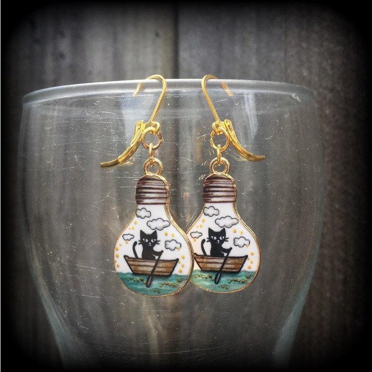 These cute quirky earrings feature a black cat rowing a little row boat down the stream under a cloudy sky. This pair of earrings can be made on your choice of hooks and clasps for pierced ears or stretched lobes.