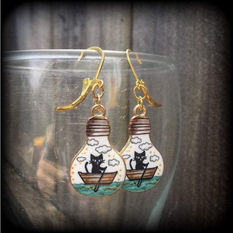 These cute quirky earrings feature a black cat rowing a little row boat down the stream under a cloudy sky. This pair of earrings can be made on your choice of hooks and clasps for pierced ears or stretched lobes.