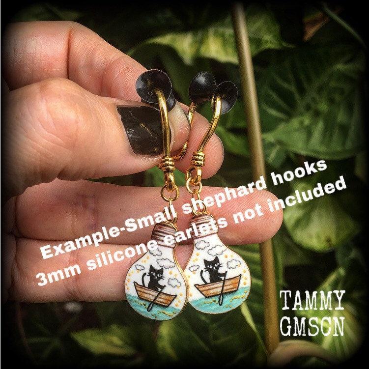 These cute quirky earrings feature a black cat rowing a little row boat down the stream under a cloudy sky. This pair of earrings can be made on your choice of hooks and clasps for pierced ears or stretched lobes.