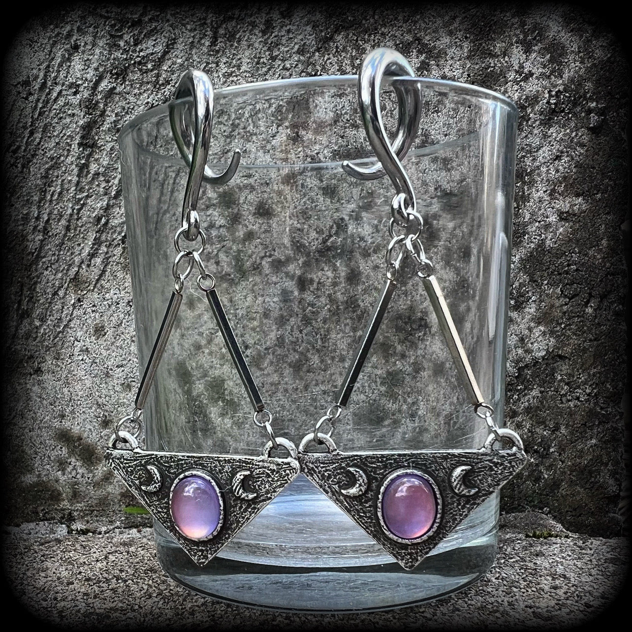 Featuring an inverted triangle with crescent moons and a single translucent purple cabachon, measuring just over 7 cms from tip to tip, and weighing approx 8 grams each.
This pair has been made on 6 gauge (4mm) surgical steel full curl hooks.