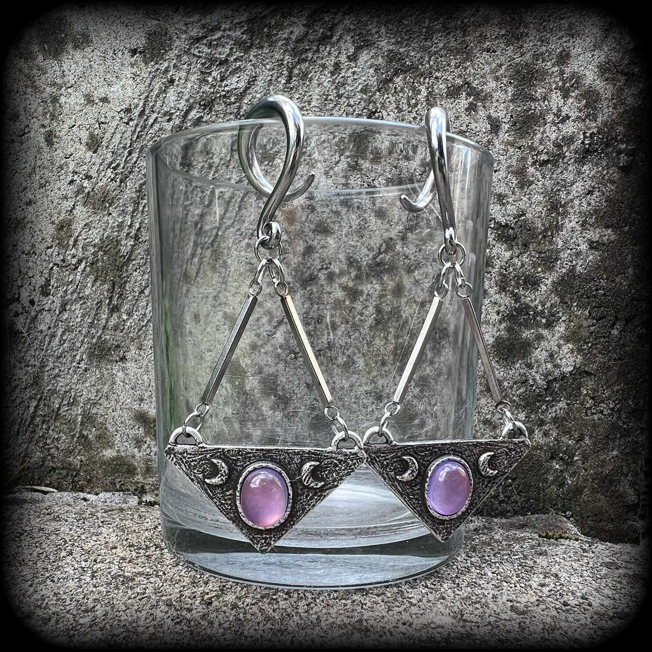 Featuring an inverted triangle with crescent moons and a single translucent purple cabachon, measuring just over 7 cms from tip to tip, and weighing approx 8 grams each.
This pair has been made on 6 gauge (4mm) surgical steel full curl hooks.