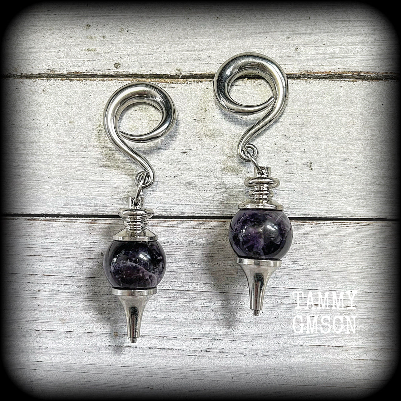 Featuring a pair of beautiful plump purple amethyst pendulums, this pair of earrings weighs approx 21 grams a piece and measure just over 7cms from tip to tip.
This pair have been made on 2 gauge (6mm) surgical steel full curl hooks, to be worn in stretched lobes.