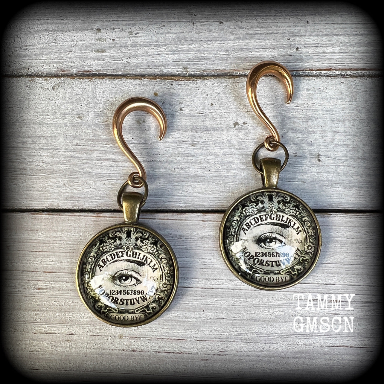 These gorgeous one of a kind Ouija board gauged earrings feature an antique bronze cabachon charm showing a classic ouija board image complete with the all seeing Mystic eye.

These earrings measure just on 6.5cms from tip to tip, and weigh approx 11 grams each.

This pair has been made on 6 gauge (4mm) stainless steel half curl hooks, suitable for stretched lobes.