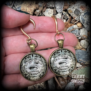 These gorgeous one of a kind Ouija board gauged earrings feature an antique bronze cabachon charm showing a classic ouija board image complete with the all seeing Mystic eye.

These earrings measure just on 6.5cms from tip to tip, and weigh approx 11 grams each.

This pair has been made on 6 gauge (4mm) stainless steel half curl hooks, suitable for stretched lobes.